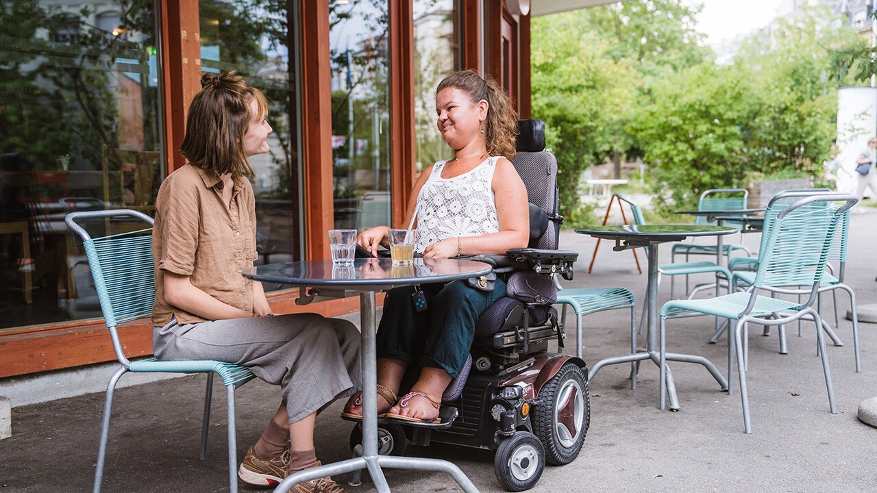 Junge Rollstuhlfahrerin mit Ihrer Assistentin in Bern in einem Café