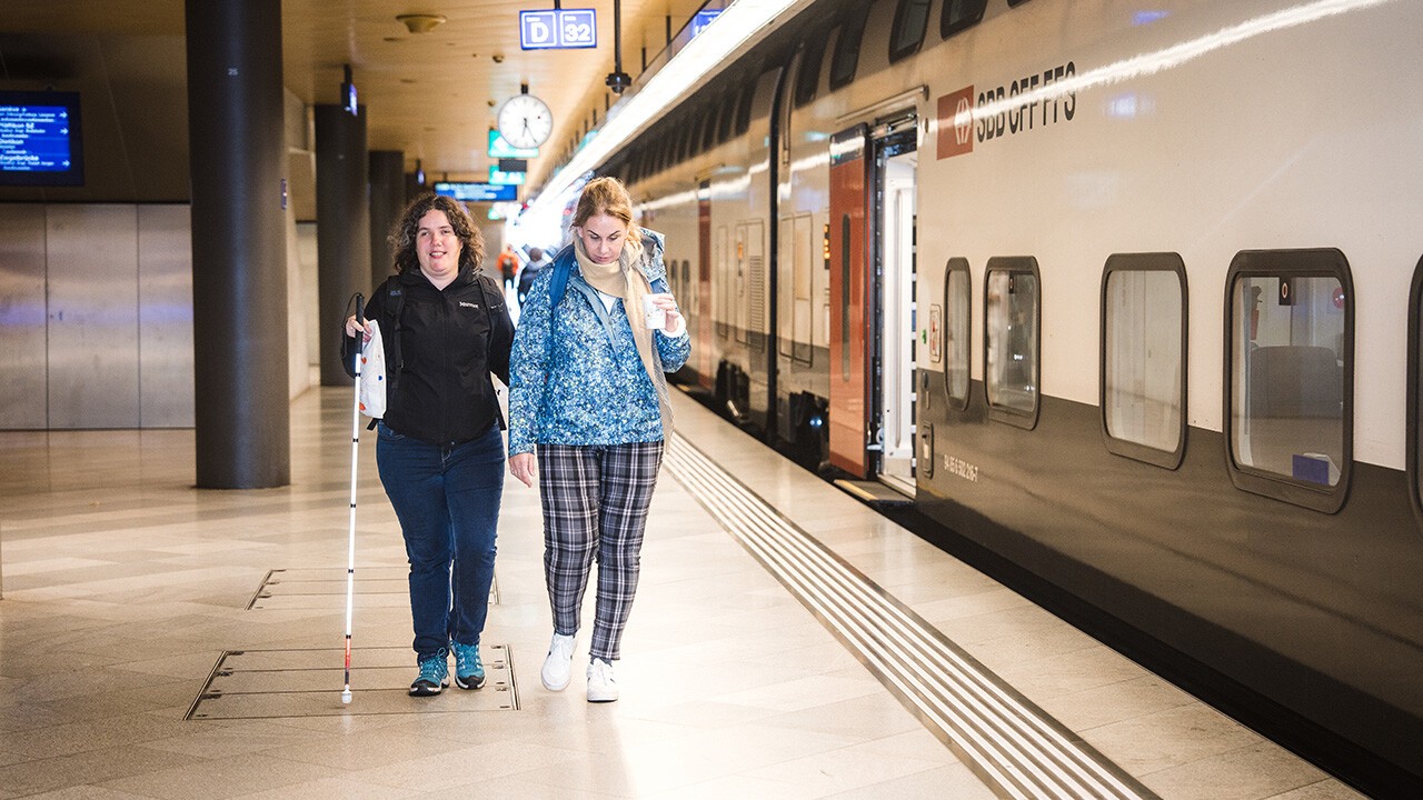 Frau mit Sehbehinderung mit ihrer Assistentin unterwegs in der Stadt 